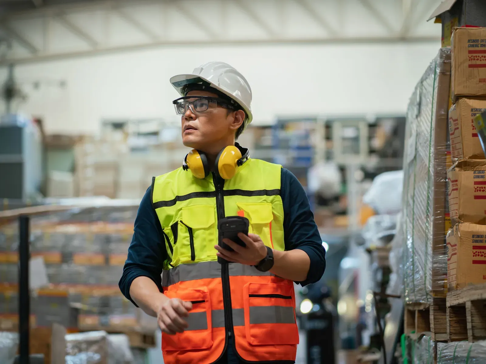 Trabajador de almacén con casco consultando un terminal móvil entre estanterías